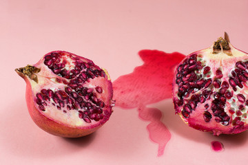 Pomegranate cut into halves. Juice leaked out on pink background