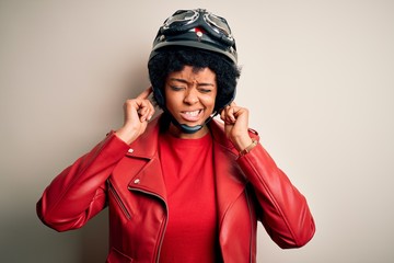 Young African American afro motorcyclist woman with curly hair wearing motorcycle helmet covering ears with fingers with annoyed expression for the noise of loud music. Deaf concept.