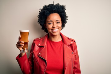 Young African American afro woman with curly hair drinking glass of beer with alcohol with a happy face standing and smiling with a confident smile showing teeth