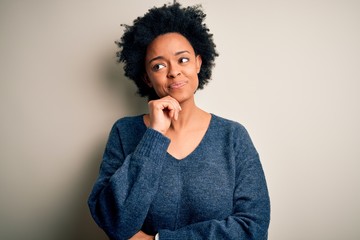 Fototapeta na wymiar Young beautiful African American afro woman with curly hair wearing casual sweater with hand on chin thinking about question, pensive expression. Smiling and thoughtful face. Doubt concept.
