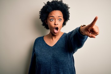 Young beautiful African American afro woman with curly hair wearing casual sweater Pointing with finger surprised ahead, open mouth amazed expression, something on the front