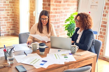 Two beautiful businesswomen smiling happy and confident. Sitting with smile on face working together using laptop at the office