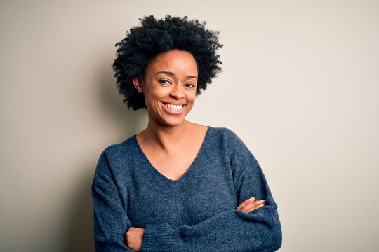 Young beautiful African American afro woman with curly hair wearing casual sweater happy face smiling with crossed arms looking at the camera. Positive person.