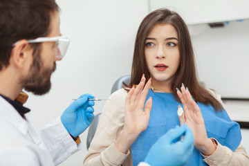 Young woman looking scared and nervous sitting in dental chair in front of her dentist. Terrified woman afraid of dental treatmentddd