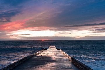 Big waves breaking on a stone pier in stormy weather with a bright sunset, a big tide. Black Sea. Sochi, February.