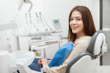 Happy beautiful woman with healthy white teeth sitting in dental chair at the clinic, copy space