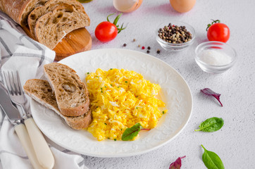 Scrambled eggs cooking from organic fresh eggs on a white plate with rye bread on a light background with a cup of coffee. Healthy breakfast. Horizontal orientation. Top view, close up