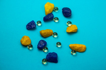 Scattered capsules, tablets near multi-colored stones on a blue background, medical concept, pharmacist