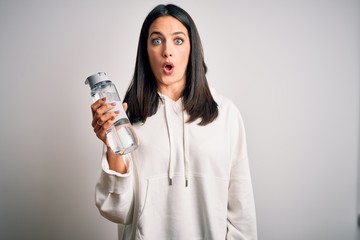 Young brunette sporty woman with blue eyes holding water bottle over white background scared in shock with a surprise face, afraid and excited with fear expression