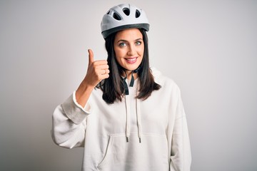 Young cyclist woman with blue eyes wearing bike helmet over isolated white background doing happy thumbs up gesture with hand. Approving expression looking at the camera showing success.