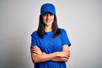 Young delivery woman with blue eyes wearing cap standing over blue background happy face smiling with crossed arms looking at the camera. Positive person.