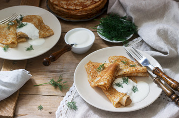 Buckwheat pancakes served with sour cream and dill on a wooden table. Rustic style.