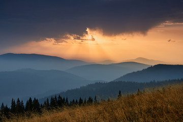 Majestic landscape of mountains at sunrise. View of the misty tops and layer hills of the mountains in the distance. Dramatic sky and rays of sunlight at morning. Concept of nature background.