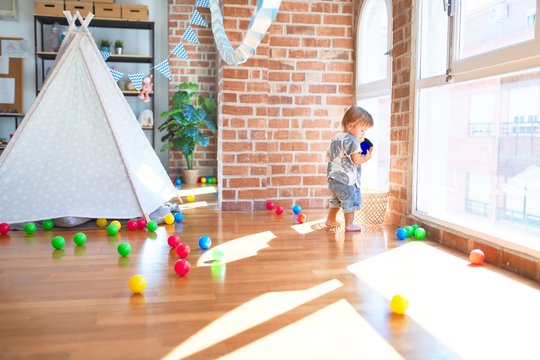 Adorable toddler playing with balls around lots of toys at kindergarten