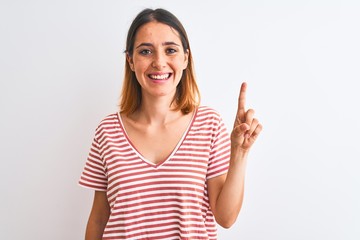 Beautiful redhead woman wearing casual striped red t-shirt over isolated background showing and pointing up with finger number one while smiling confident and happy.