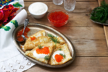 Homemade pancakes with red caviar, sour cream and dill served with vodka. Rustic style.