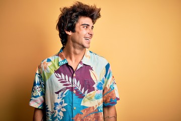 Young handsome man on vacation wearing summer shirt over isolated blue background looking away to side with smile on face, natural expression. Laughing confident.