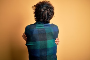 Young handsome man wearing casual shirt standing over isolated yellow background Hugging oneself...