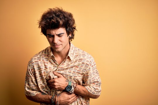 Young handsome man on vacation wearing summer shirt over isolated yellow background with hand on stomach because nausea, painful disease feeling unwell. Ache concept.