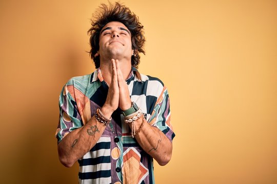 Young handsome man on vacation wearing summer shirt over isolated yellow background begging and praying with hands together with hope expression on face very emotional and worried. Begging.
