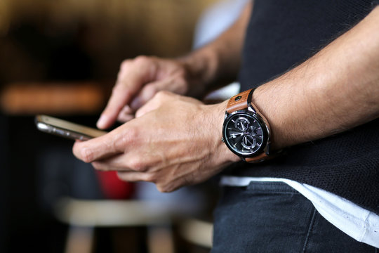 Man checking his smartphone while wearing a stylish wrist hand watch. Technology and class concept. Modern mobile phone. Social media and business person