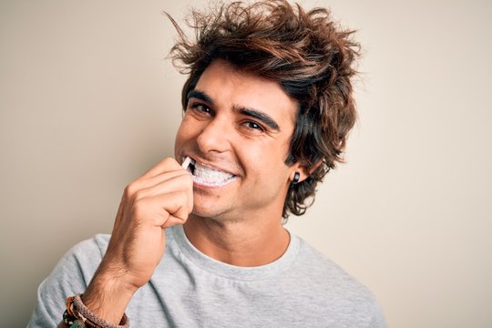 Young handsome man smiling happy. Standing with smile on face whasing tooth using toothbrush over isolated white background