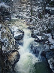 River runs through the frozen rocks of the mountain. Winter landscape with cool tones, showing snow and ice.