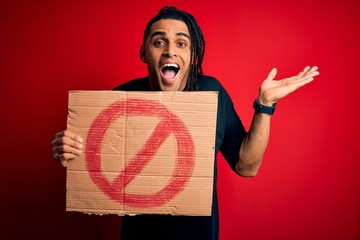 Young handsome african american man with dreadlocks holding banner with prohibited signal very...