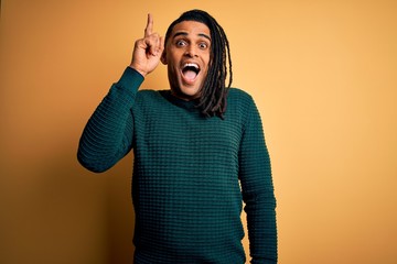 Young handsome african american afro man with dreadlocks wearing green casual sweater pointing finger up with successful idea. Exited and happy. Number one.