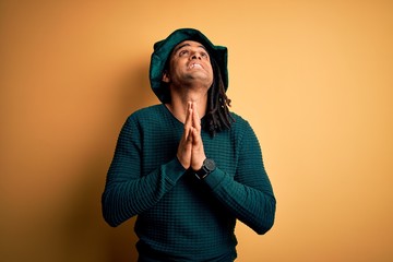 Young african american man wearing green hat with clover celebrating saint patricks day begging and praying with hands together with hope expression on face very emotional and worried. Begging.