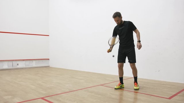 A portrait of a young bearded man serving the ball in the squash cort