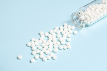 Homeopathic globules scattered from a clear glass bottle on light blue background, alternative homeopathy medicine concept