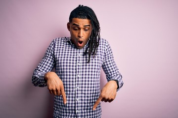 Young handsome african american afro man with dreadlocks wearing casual shirt Pointing down with fingers showing advertisement, surprised face and open mouth