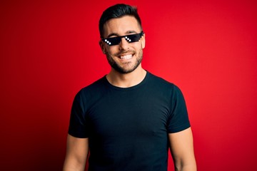 Young handsome man wearing funny thug life sunglasses over isolated red background with a happy and...