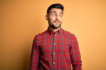 Young handsome man wearing casual shirt standing over isolated yellow background smiling looking to the side and staring away thinking.