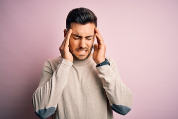 Young handsome man wearing casual sweater standing over isolated pink background with hand on head for pain in head because stress. Suffering migraine.