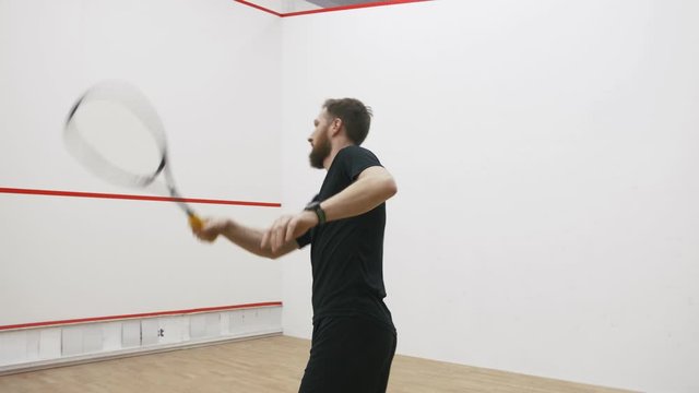 A portrait of a young bearded man practicing to play squash, slow motion