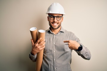 Young architect man wearing contractor helmet holding project paper plan over isolated background with surprise face pointing finger to himself - obrazy, fototapety, plakaty