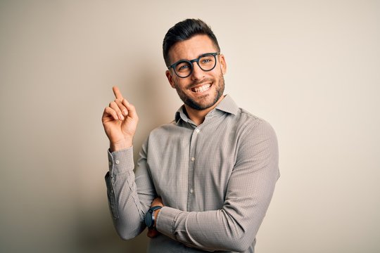 Young handsome man wearing elegant shirt and glasses over isolated white background with a big smile on face, pointing with hand and finger to the side looking at the camera.