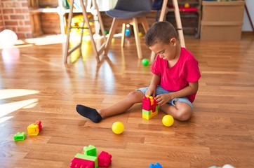Adorable toddler playing with building blocks around lots of toys at kindergarten