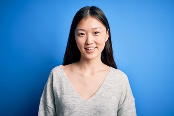 Obraz premium Young beautiful asian woman wearing casual sweater standing over blue isolated background with a happy and cool smile on face. Lucky person.