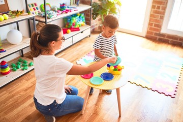 Beautiful toddler boy sitting on puzzle playing with plastic plates, fruits and vegetables at...