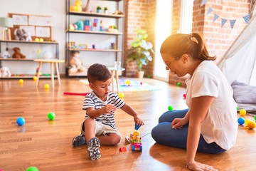Fototapeta premium Beautiful teacher and toddler boy playing with train at kindergarten