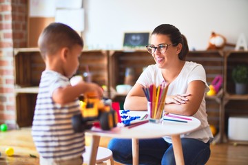 Beautiful teacher and toddler boy playing with tractor and cars at kindergarten