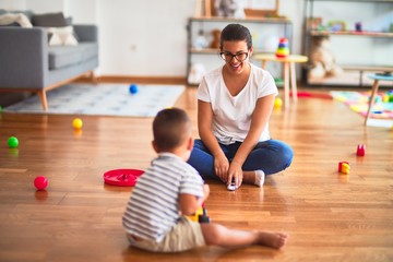 Fototapeta premium Beautiful teacher and toddler boy playing with tractor and cars at kindergarten