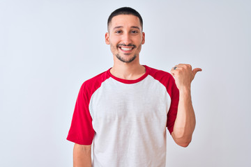 Young handsome man standing over isolated background smiling with happy face looking and pointing to the side with thumb up.