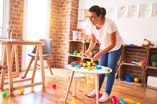 Beautiful teacher and toddler boy playing with construction blocks bulding tower at kindergarten