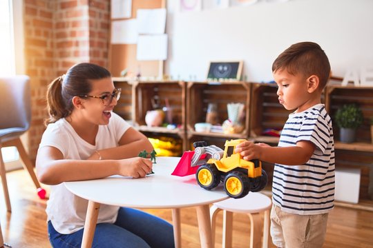 Beautiful teacher and toddler boy playing with tractor and cars at kindergarten