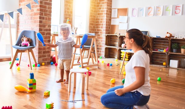 Beautiful teacher and toddler boy playing with plastic basket at kindergarten