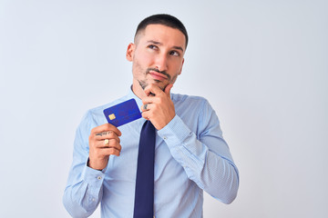 Young business man holding credit card over isolated background serious face thinking about question, very confused idea